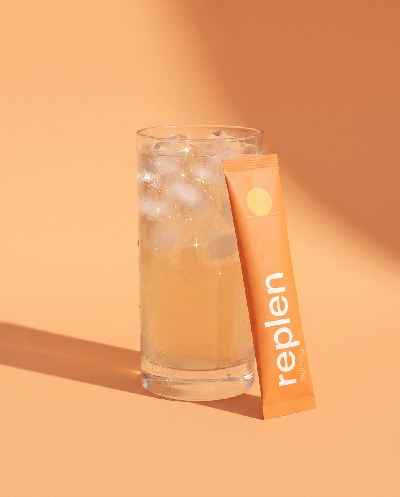 A tall glass of pale apricot drink with ice, the orange morning stick leaning against it