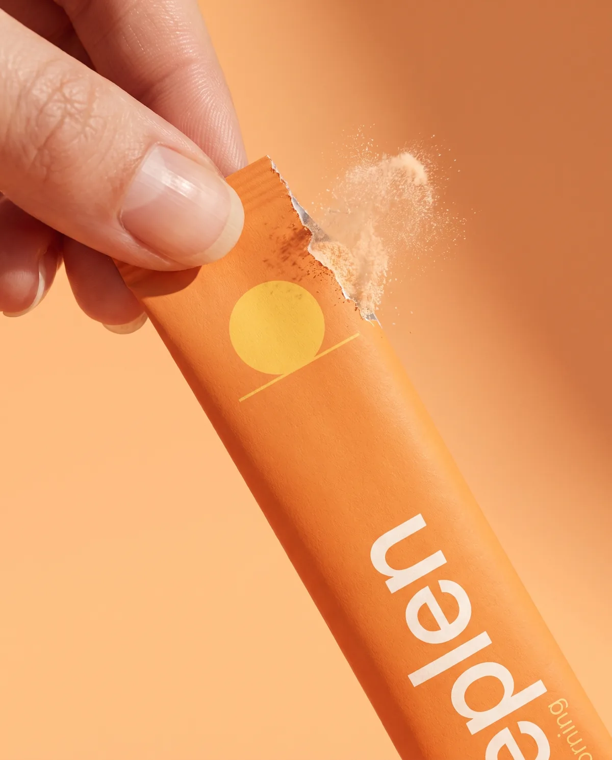 Two fingertips tearing open the orange morning stick, a puff of powder escaping